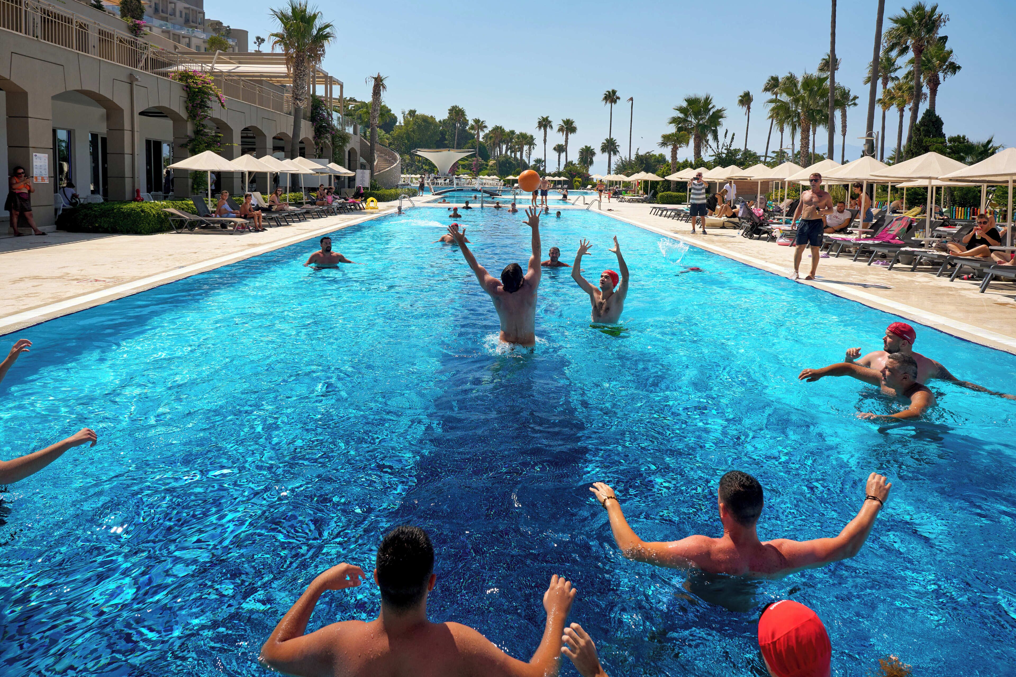 Une piscine où des gens s’amusent, entourée de palmiers et de chaises longues.