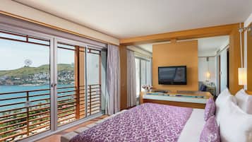 Quarto de hotel com cama, televisão, escrivaninha e varanda com vista para o mar.