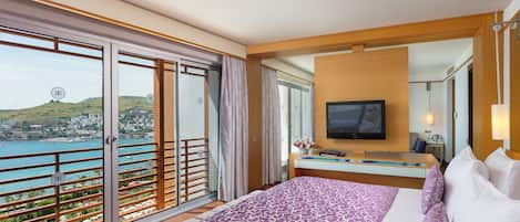 Ett hotellrum med en säng, en TV, ett skrivbord och en balkong med utsikt över havet.