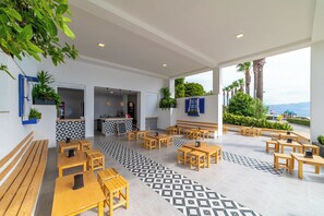 A spacious outdoor seating area with wooden tables and benches, a patterned floor, and a view of the sea. - Kefaluka Resort - All Inclusive (Bodrum)