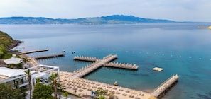 A coastal resort with a pier extending into calm waters, surrounded by beachside amenities and a mountainous backdrop.