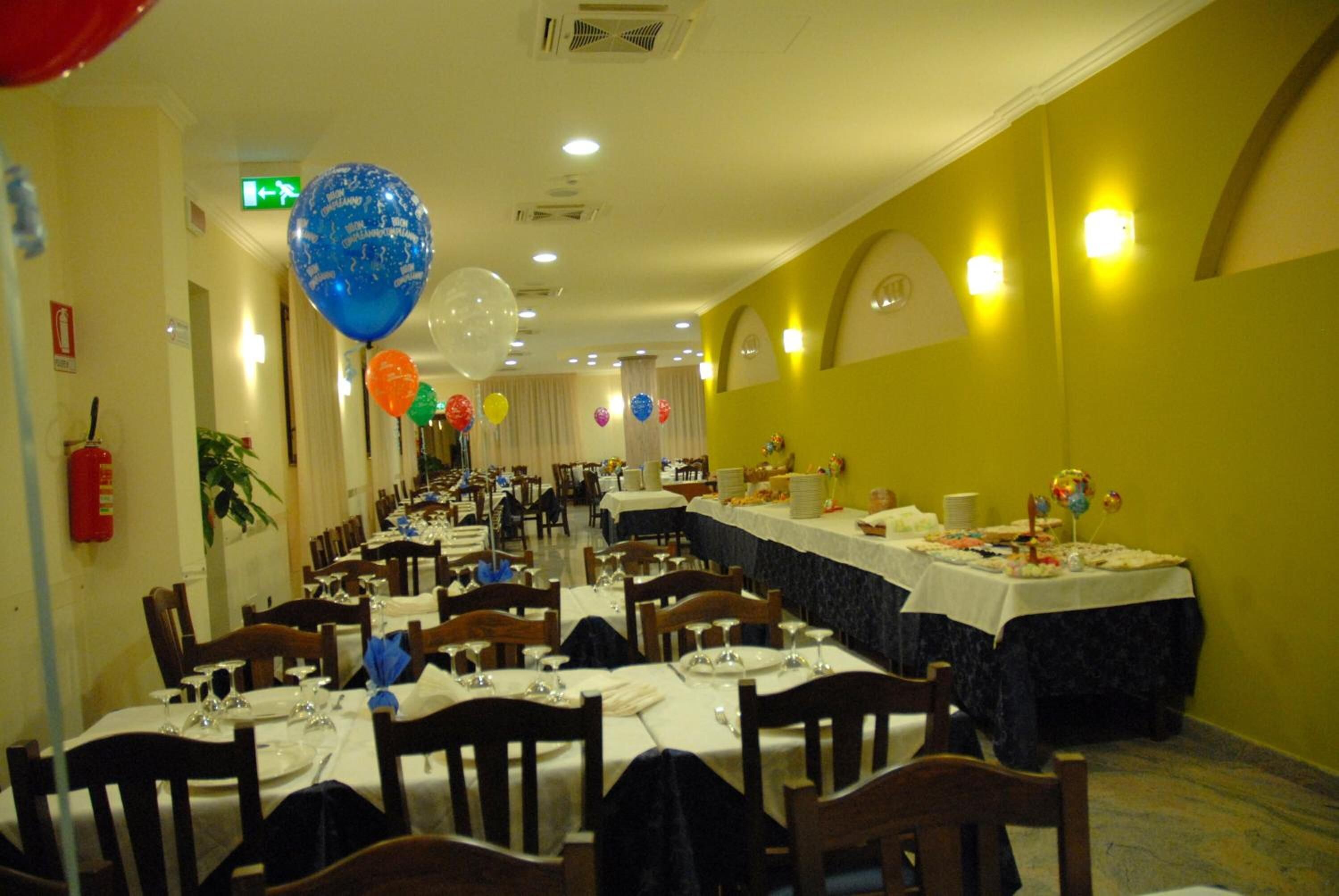 Ein Festsaal mit festlich gedeckten Tischen, darunter ein langer Tisch mit weißer Tischdecke und dunklem Überwurf.