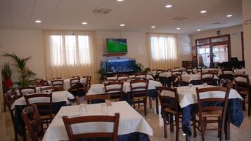 Un comedor con varias mesas y sillas, un televisor montado en la pared y una ventana con cortinas.