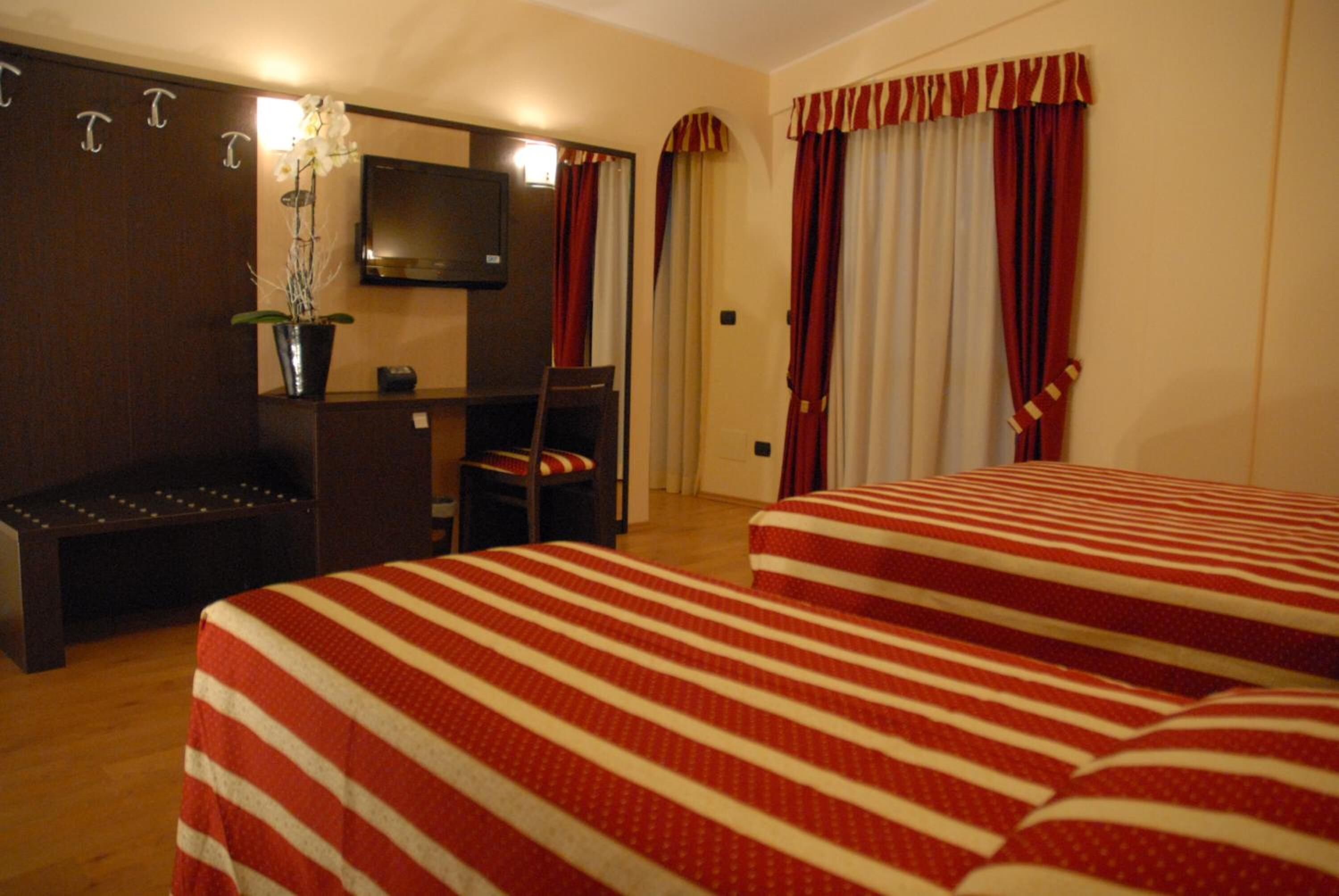 Een hotelkamer met twee bedden, een bureau, een stoel, een televisie en een potplant.