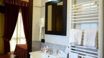 A hotel bathroom with a sink, mirror, towel rack, and a window with curtains.