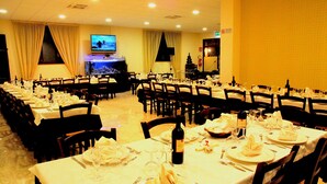 A banquet hall with multiple tables set for dining, a television screen, and a Christmas tree. - Iacone (Chieti)