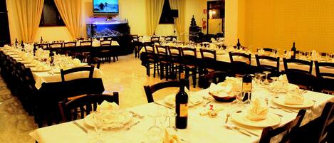 Un salón de banquetes con varias mesas dispuestas para comer, una pantalla de televisión y un árbol de Navidad.