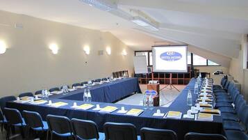 Une salle de conférence avec une longue table, des chaises et un écran de projection sur lequel est affiché le mot « HÔTEL LACONE ».