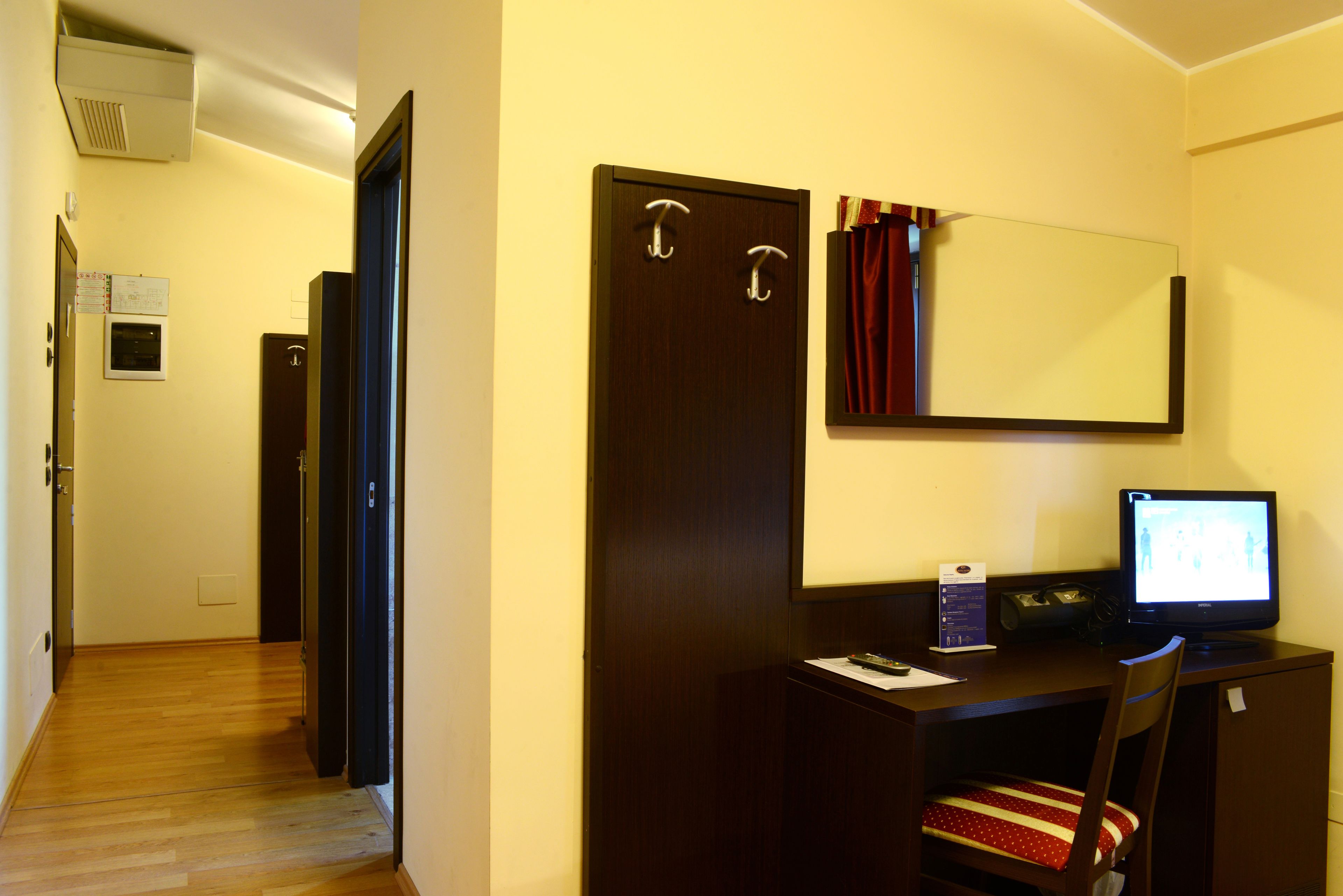 Habitación de hotel con un escritorio de madera, una computadora, una silla, un espejo y una puerta.