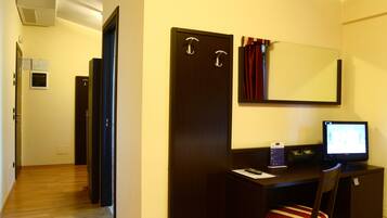 Habitación de hotel con un escritorio de madera, una computadora, una silla, un espejo y una puerta.
