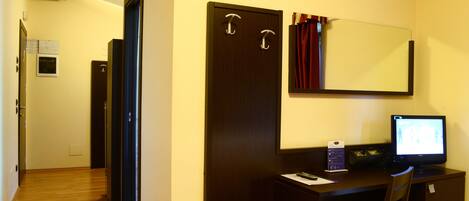 A hotel room with a wooden desk, a computer, a chair, a mirror, and a door.
