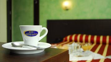 Eine weiße Tasse mit einem Logo auf einem Holztisch, daneben ein Löffel, im Hintergrund ein Bett mit einer gestreiften Decke.