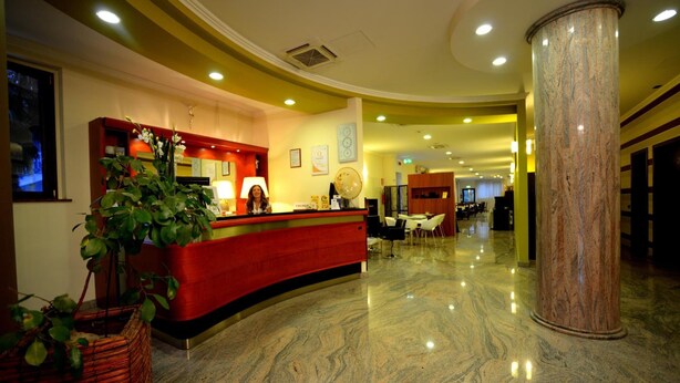 A hotel reception area with a curved red counter, a large marble column, and a reception desk. - Iacone (Chieti)