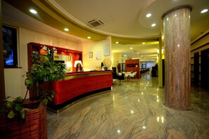 A hotel reception area with a curved red counter, a large marble column, and a reception desk. - Iacone (Chieti)