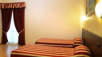 A hotel room with two beds, a window with curtains, and a wall-mounted light fixture.