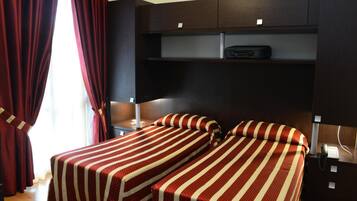 A hotel room with two beds, a desk, and a wardrobe.