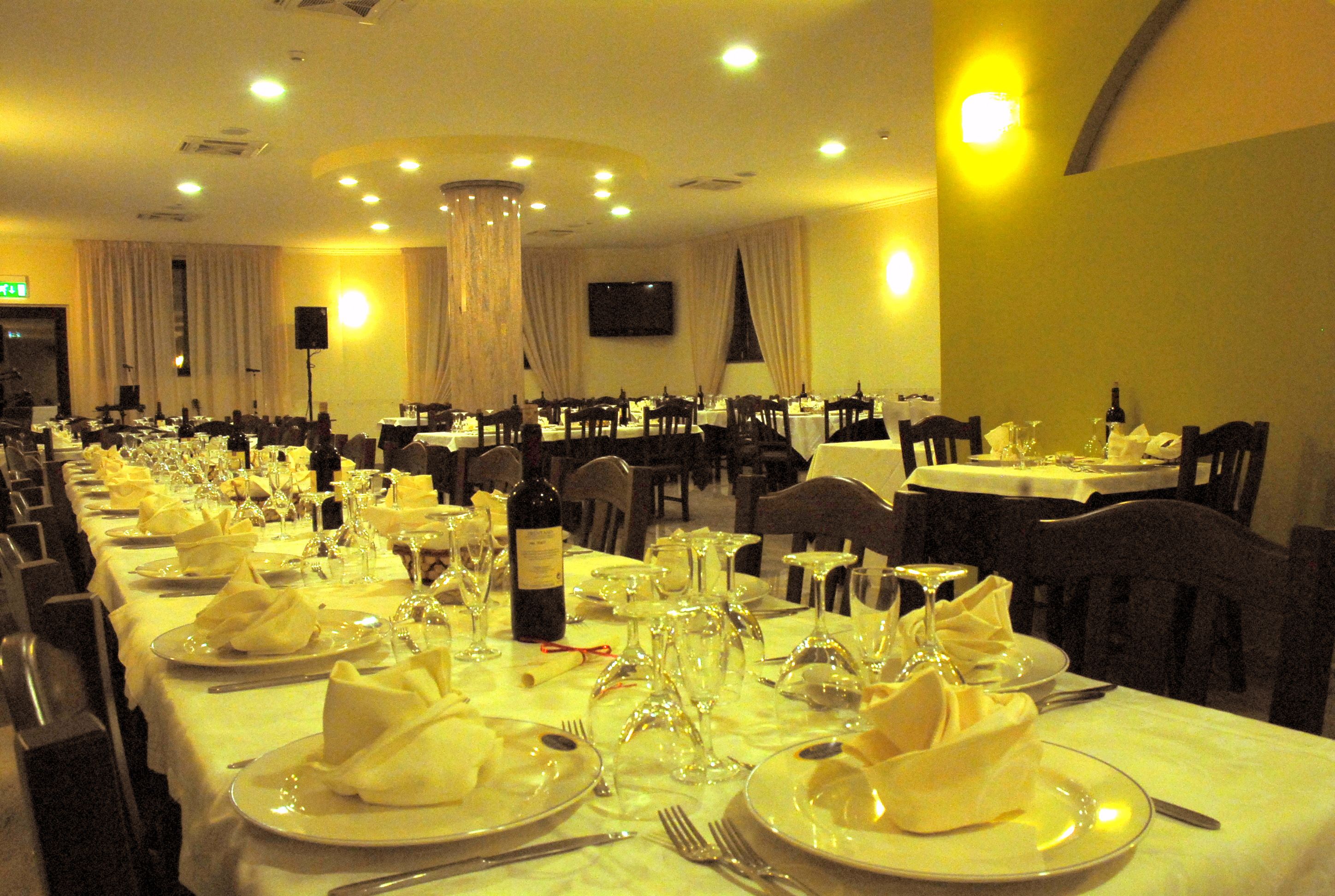 Un salón de banquetes con varias mesas redondas dispuestas para cenar, cada una con manteles blancos, platos, cubiertos y copas de vino.