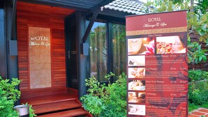 L’entrée d’un spa, avec une façade en bois, une poubelle en métal et un panneau d’affichage détaillé présentant les différents services proposés, tels que les massages et l’aromathérapie.