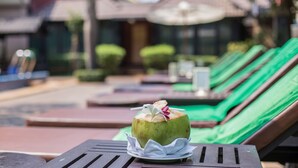 Une boisson à base de noix de coco, posée sur une table en bois avec une serviette, entourée de chaises longues et de parasols, dans un cadre de station balnéaire.