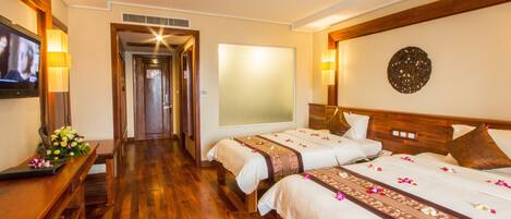 Habitación de hotel con dos camas, suelo de madera, televisor, escritorio con lámpara y un adorno en la pared.