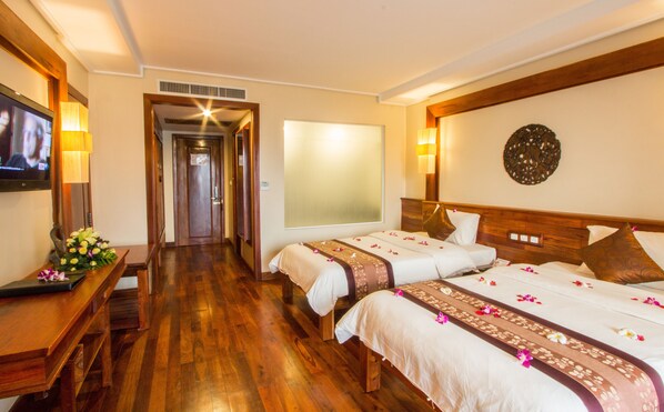 Habitación de hotel con dos camas, suelo de madera, televisor, escritorio con lámpara y un adorno en la pared.
