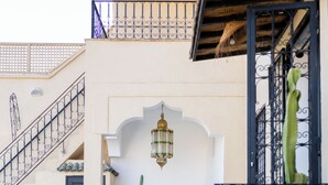 A narrow courtyard with a tiled floor, a cactus, a lantern, and a staircase with a railing.
