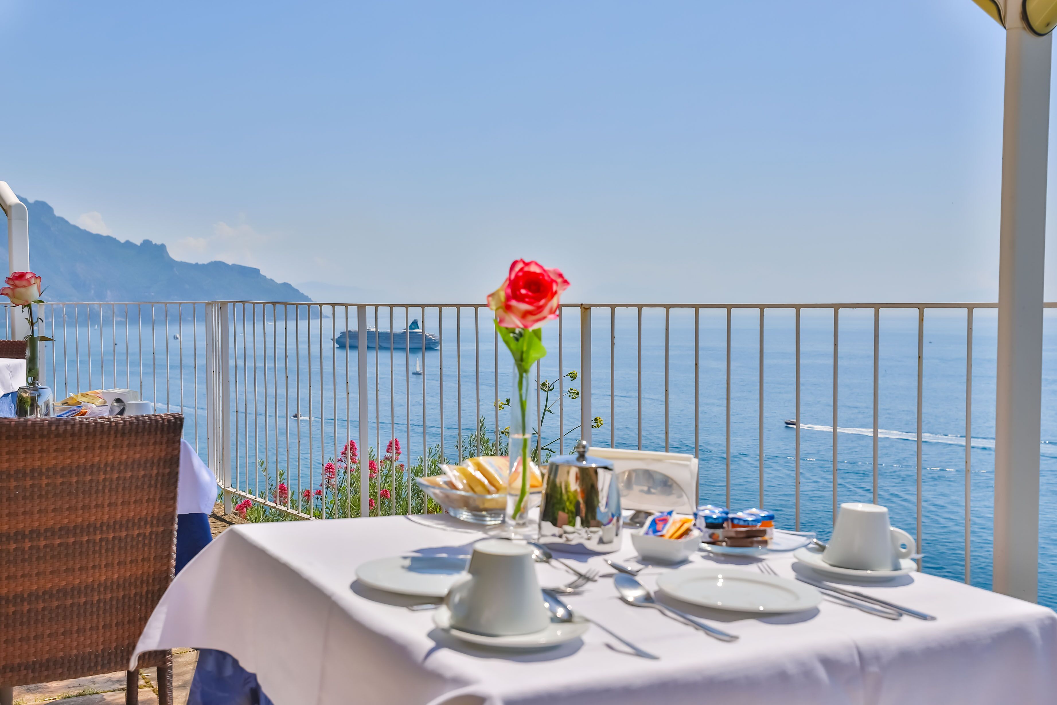 Une table dressée pour deux personnes, avec une vue sur la mer et les montagnes en arrière-plan.