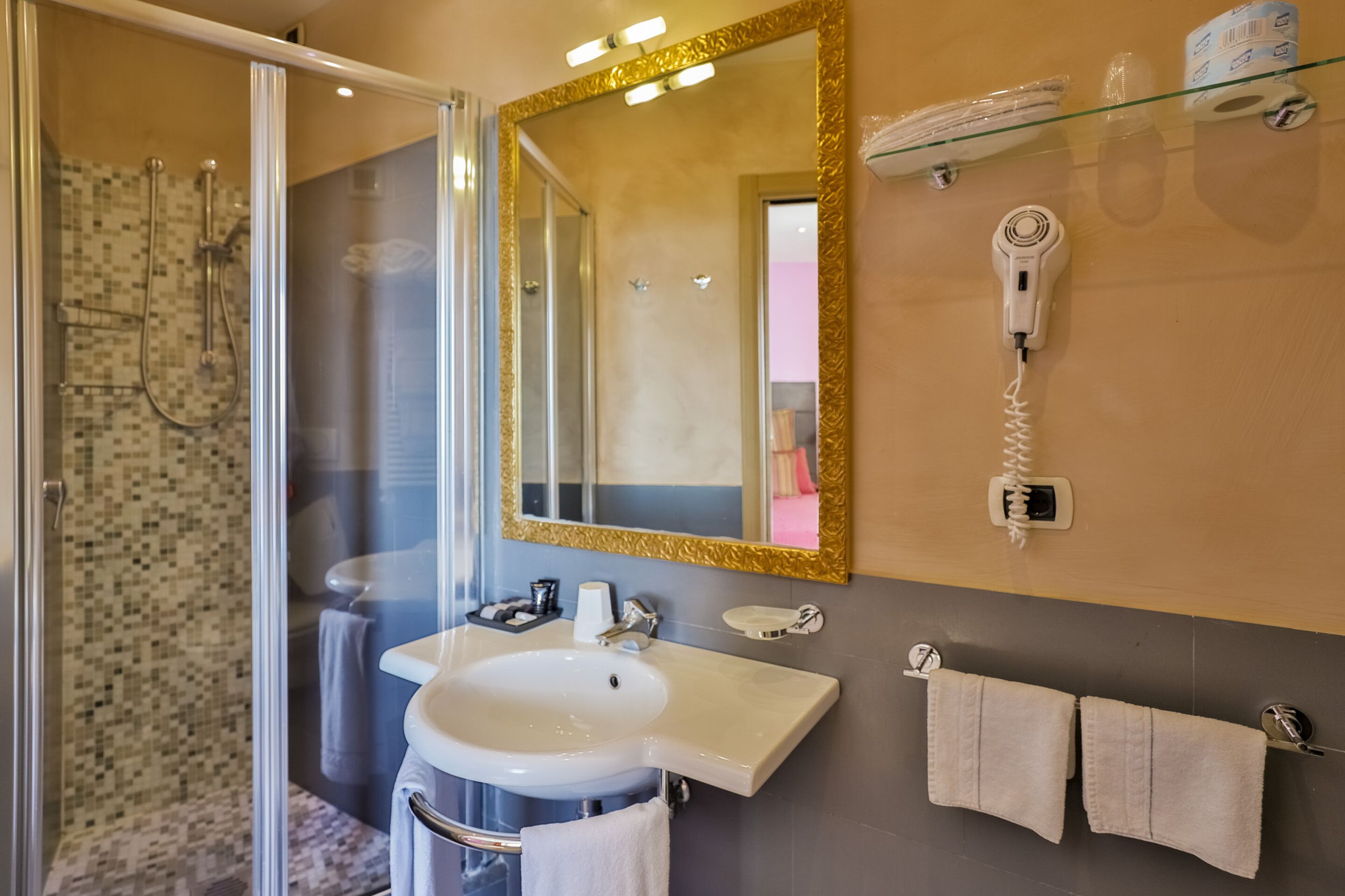 Un baño con cabina de ducha de vidrio, lavamanos, espejo y perchero.