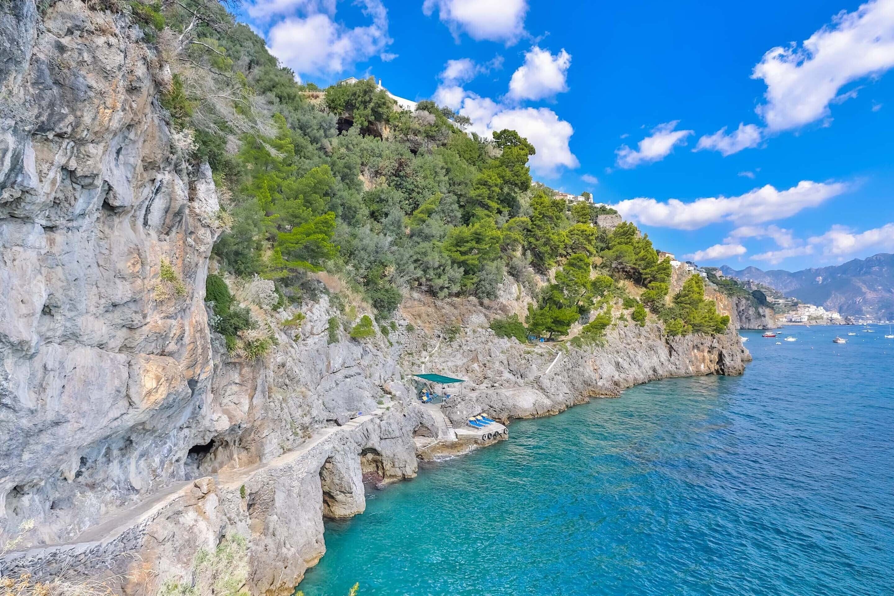 A coastal road with rocky cliffs and a clear blue sea.