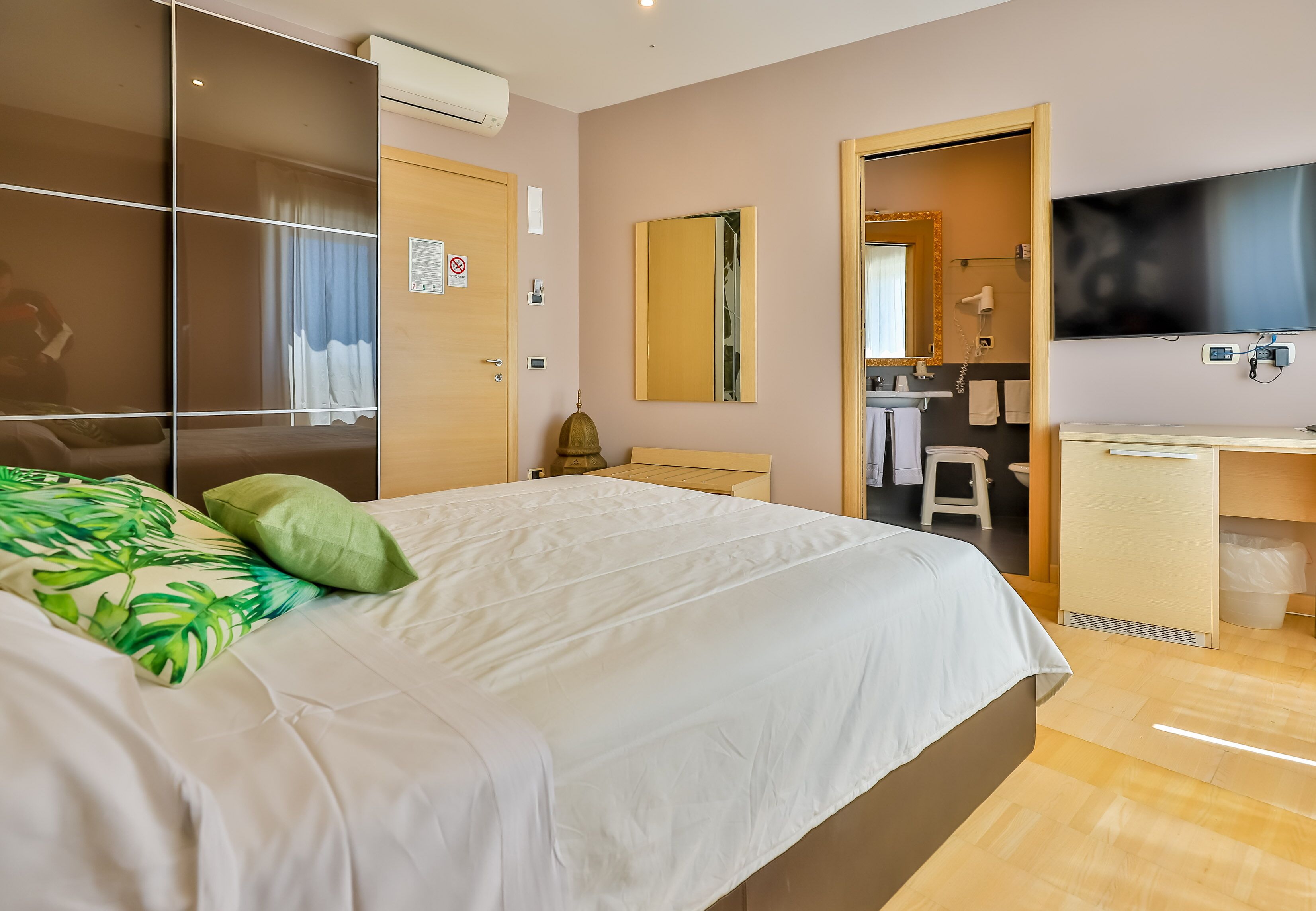 Habitación de hotel con cama, escritorio, televisor y baño visible a través de una puerta abierta.