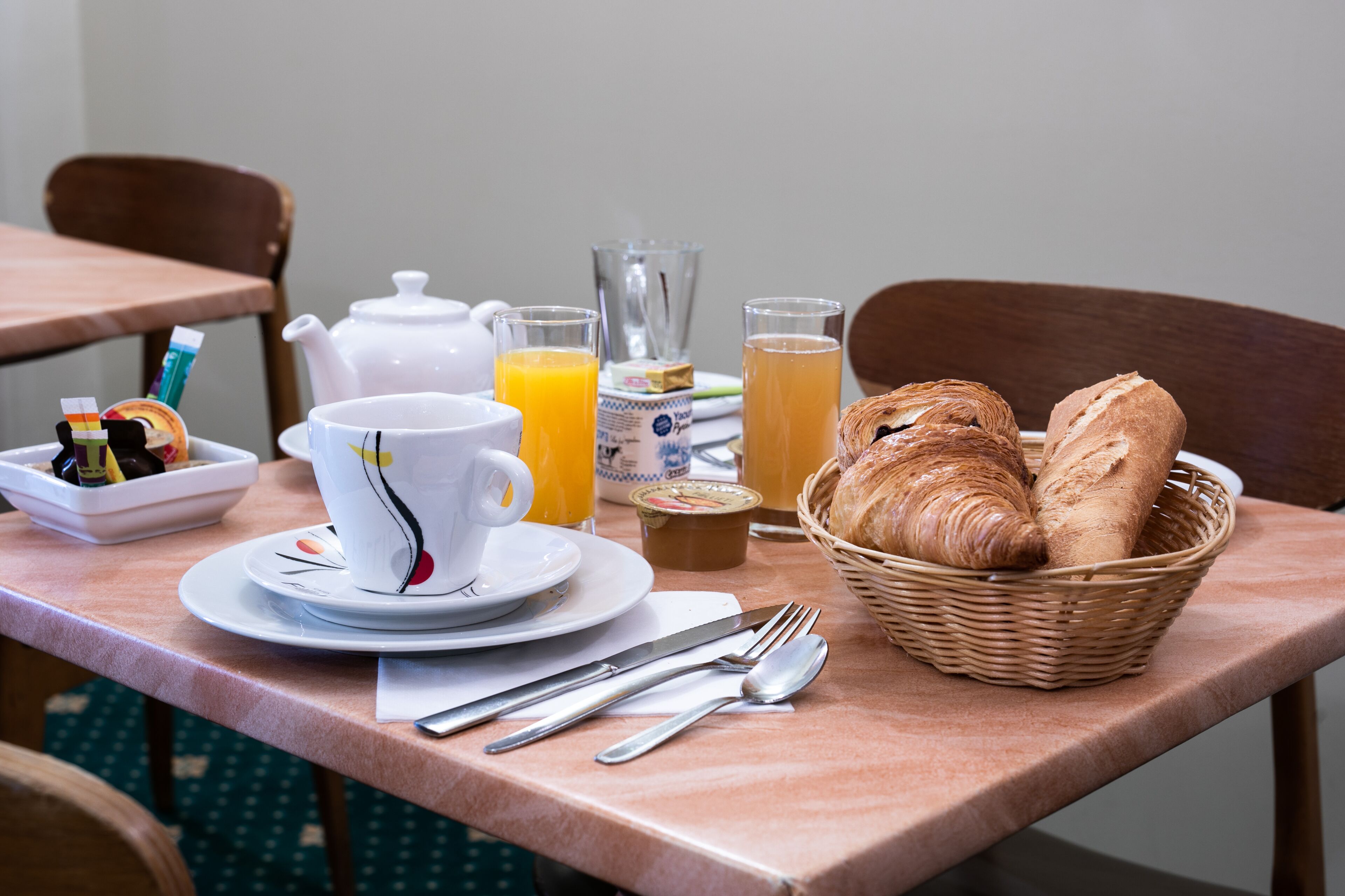 Ein Frühstückstisch mit Croissants, Saft, einem Teekessel und einer Tasse.