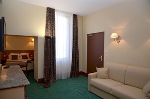 A hotel room with a bed, a sofa, a desk with a lamp, and a window with curtains. - Hôtel Héliot, Cosy Places by Charme & Caractère (Toulouse)