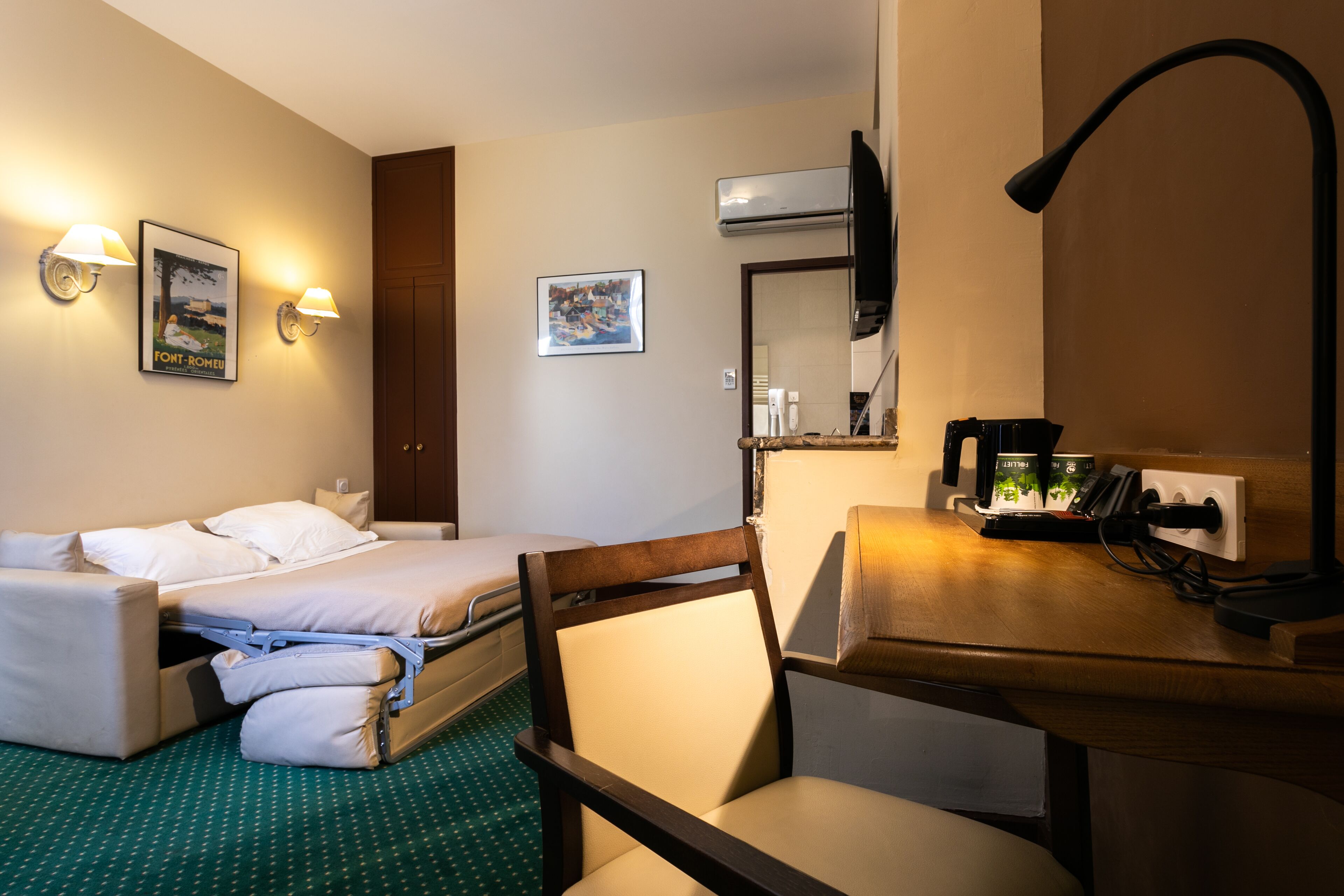 Hotelkamer met twee bedden, een bureau met lamp, een stoel en een tv aan de muur.