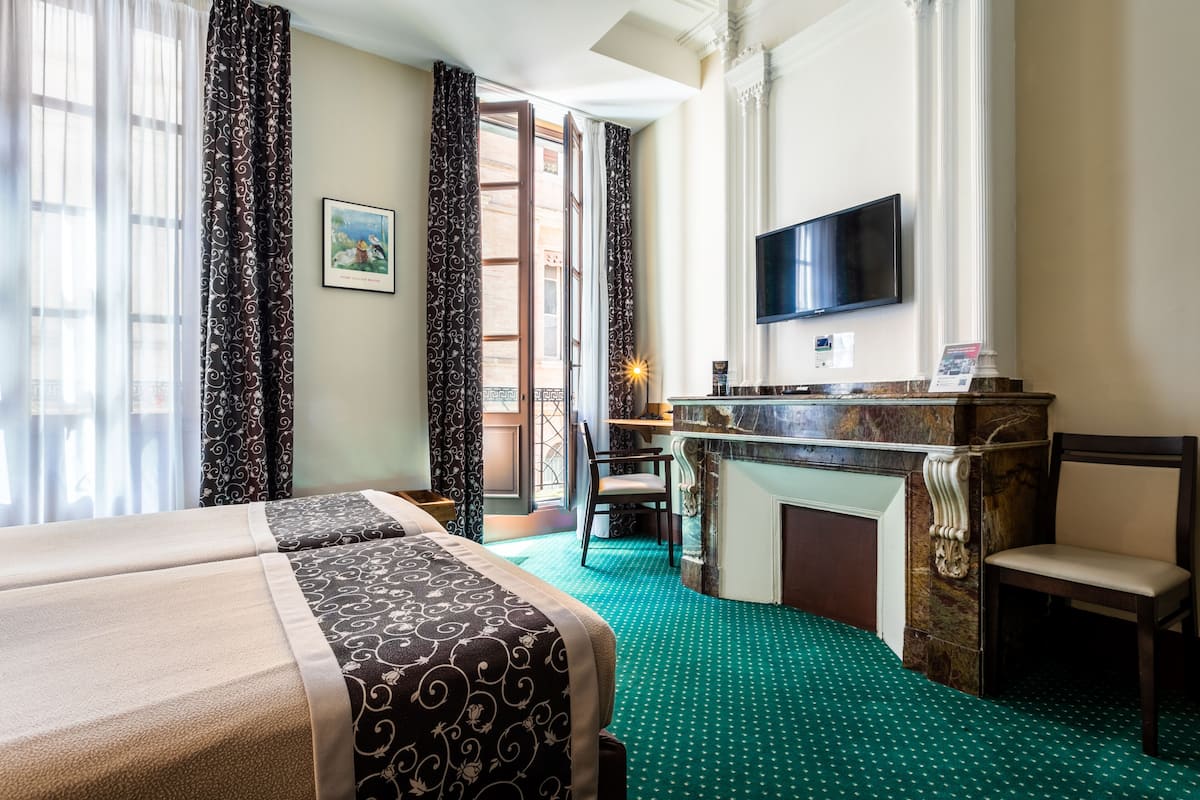 A hotel room with a bed, a desk with a flat-screen TV, a fireplace, and a view of the outside.
