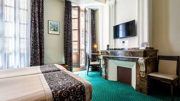 A hotel room with a bed, a desk with a flat-screen TV, a fireplace, and a view of the outside.