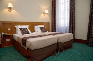A hotel room with two beds, a wooden headboard, two bedside lamps, a telephone, and a green carpet.