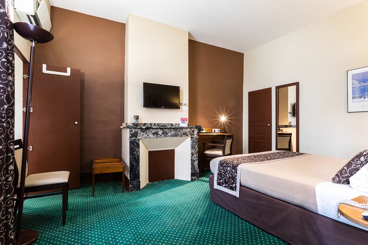A hotel room with a bed, a desk with a chair, a television, a fireplace, and a mirror.