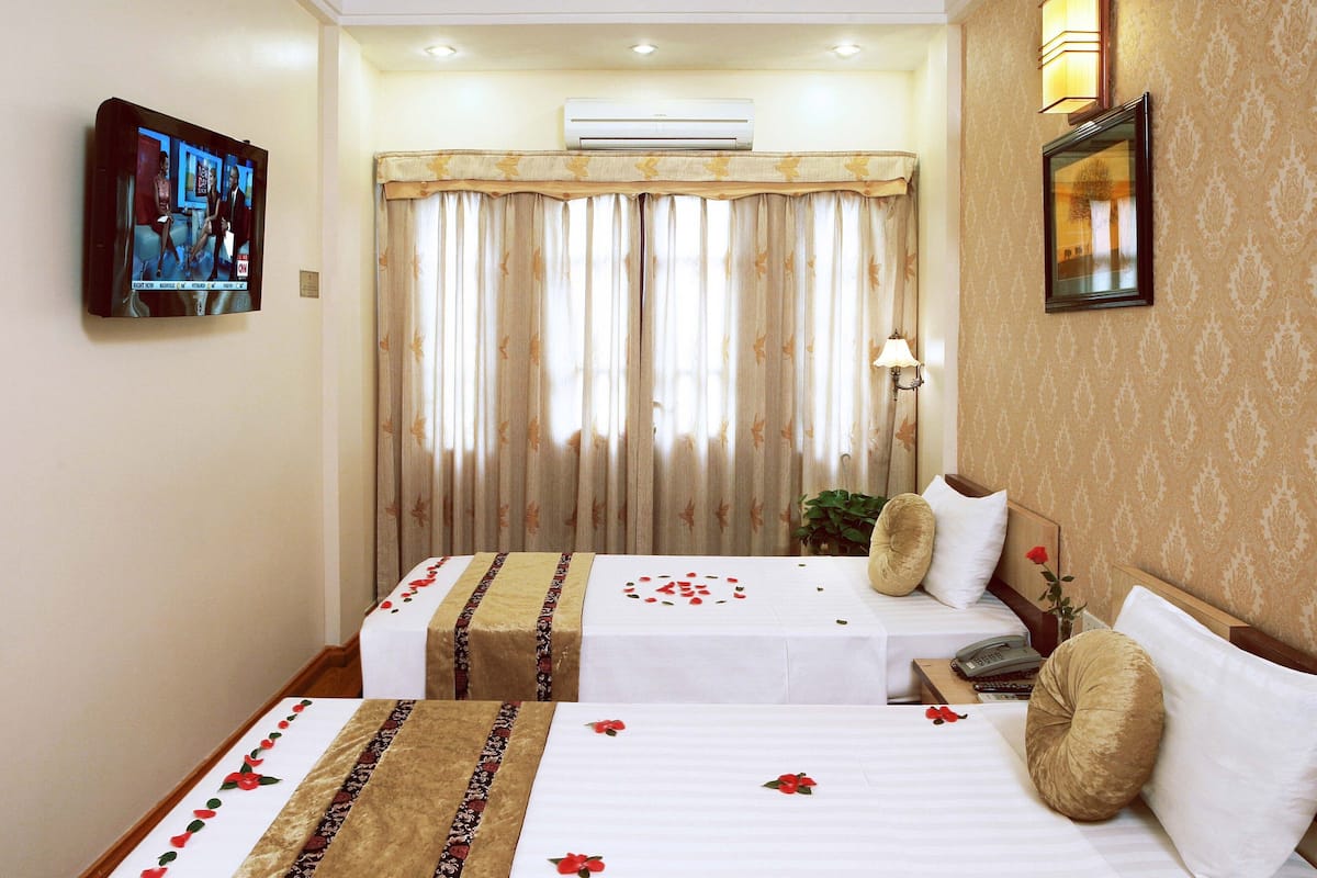 A hotel room with two beds, a television, an air conditioner, and a decorative lamp.