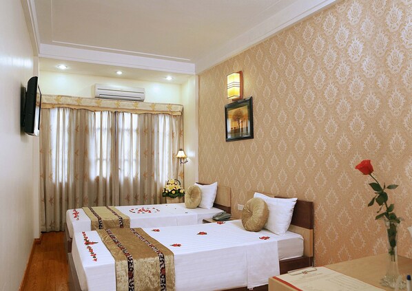 Habitación de hotel con dos camas, un televisor de pantalla plana, aire acondicionado, una lámpara de pared y un cuadro enmarcado.
