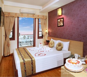 A hotel room with a bed, a view of buildings, a wall-mounted phone, and a cake on the table. - Hanoi Culture Hostel (Hanoi)