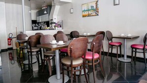 A restaurant with round tables and chairs, a kitchen in the background, and a painting on the wall. - Hotel Bonsejour Montmartre (Paris)