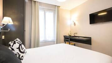 Ein Hotelzimmer mit Bett, Schreibtisch mit Stuhl, flachbildfernseher an der Wand und Fenster mit Vorhängen.
