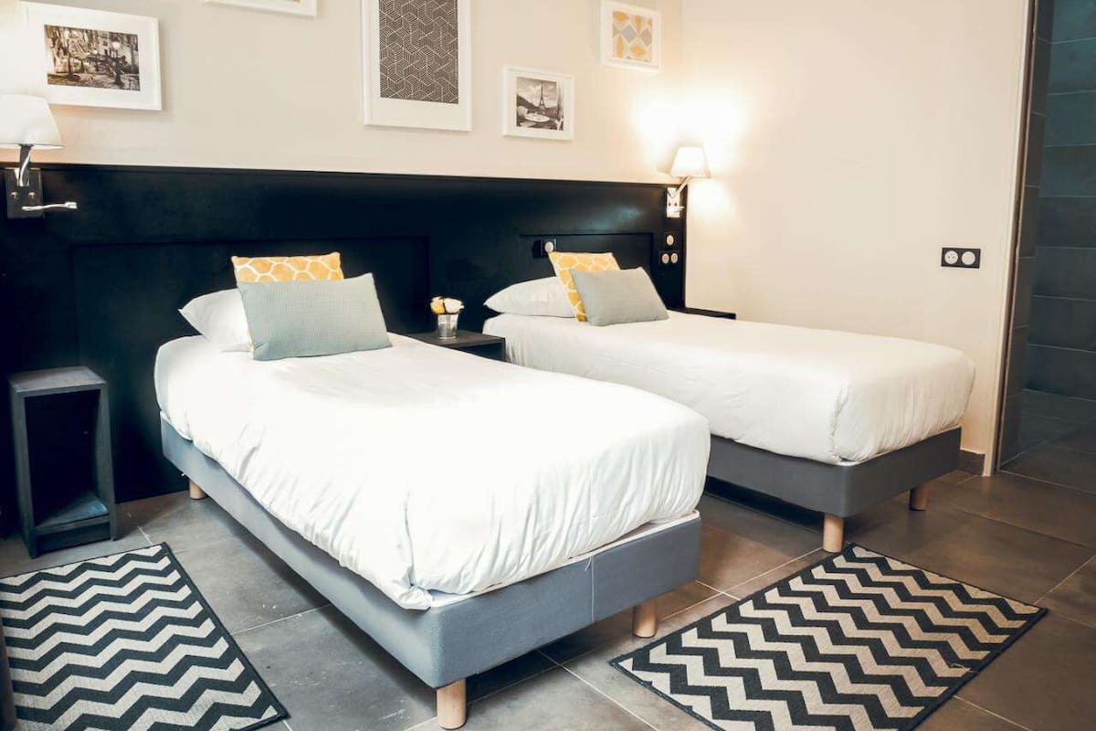Une chambre d’hôtel avec deux lits, une tête de lit noire et un mur orné de tableaux.
