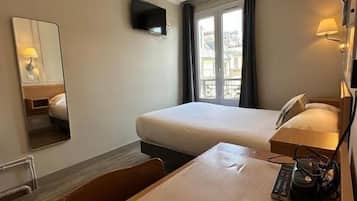 Une chambre d’hôtel avec deux lits, un bureau avec une machine à café, une télévision et une fenêtre avec des rideaux.
