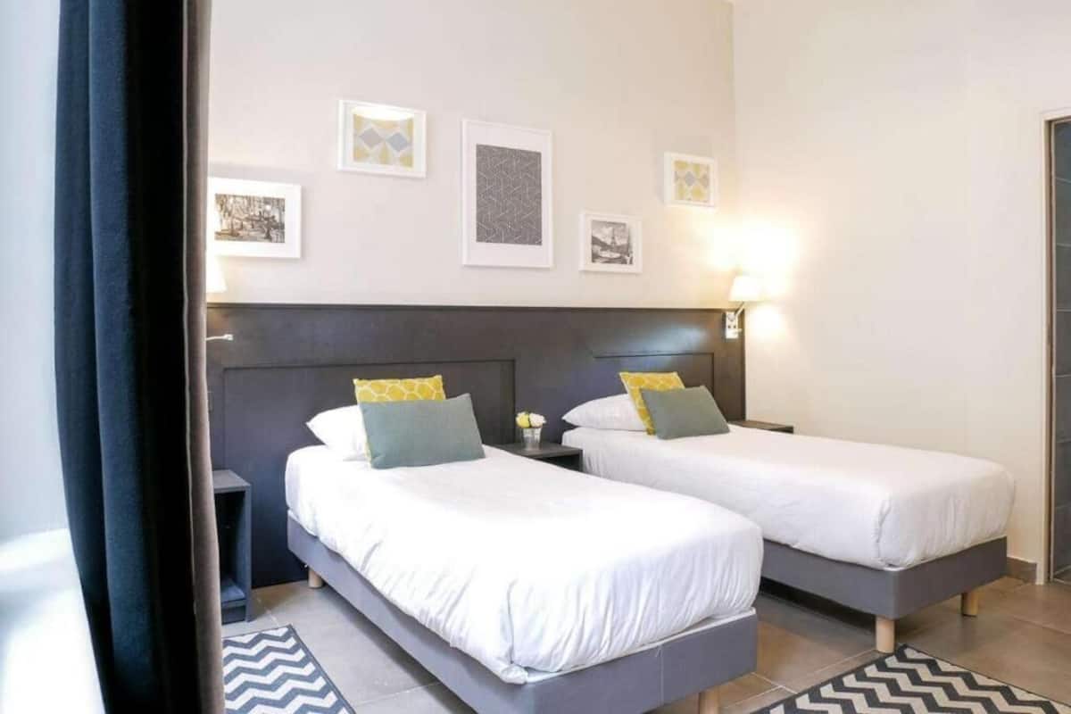 Une chambre d’hôtel avec deux lits, une tête de lit, des œuvres d’art murales et une table de chevet.