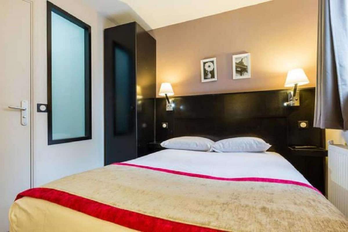 Une chambre d’hôtel avec un lit, deux lampes de chevet, une tête de lit et deux tableaux encadrés accrochés au mur.