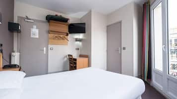 A hotel room with a large bed, a desk with a chair, a flat-screen TV mounted on the wall, and a window with colorful curtains.