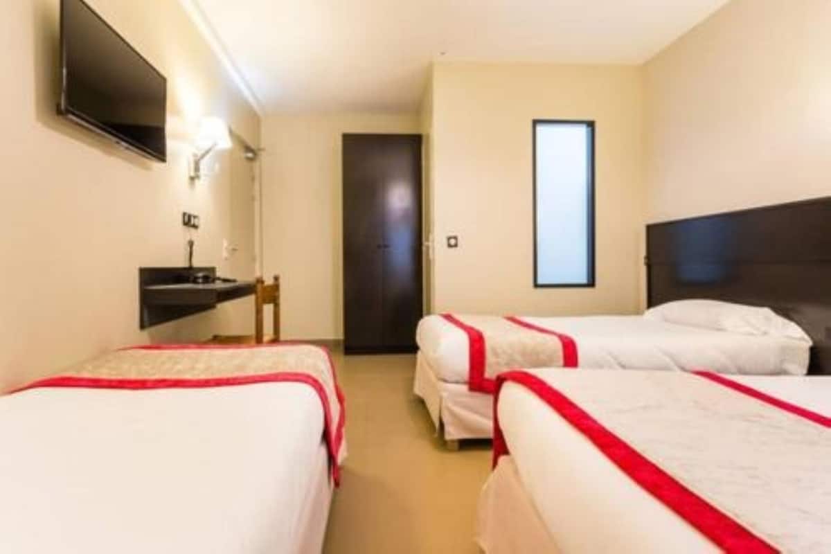 Une chambre d’hôtel avec deux lits simples, un téléviseur fixé au mur, un petit bureau avec une chaise et une porte donnant sur une autre chambre.