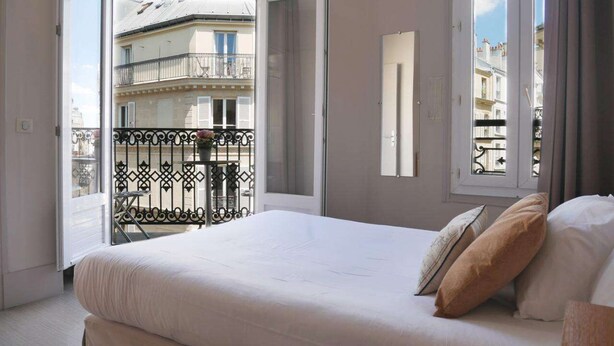 A bedroom with a large bed, a balcony with a wrought iron railing, and a view of buildings outside. - Hotel Bonsejour Montmartre (Paris)