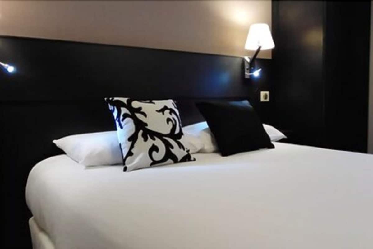Un lit bien fait, avec des oreillers blancs et noirs, une tête de lit sombre et une lampe de chevet.